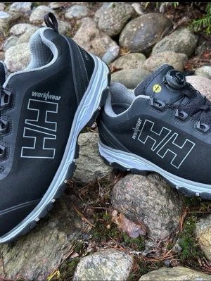 Svarta Helly Hansen workwear(43)Arbetsskor,Skyddsskor  - Du kollar på ett par riktigt schysta arbetsskor av kvalitetsmäket Helly Hansen i strl 43.   Sparsamt använda på fot en kortare tid så skorna är givetvis i mycket bra skick.   Vattentät skyddssko som påminner om ett par helt vanliga sneakers skor.  Bra dämpning i kombination med bra stöd runt om och under fot.   Denna modell tillför en bredare läst in i Chelsea Evolution-serien. Exceptionell komfort och en slitstark ovandel i mikrofiber i kombination med en vattentät lösning- HellyTech membran, g