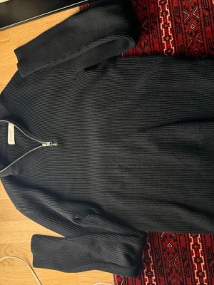 Svart ribbad polotröja Jack & Jones - Svart polotröja från Jack & Jones med ribbad struktur och half zip-dragkedja vid halsen. Tröjan är långärmad och har en hög krage som ger en cool look. Perfekt för dig som gillar stilrena och enkla plagg med lite edge.