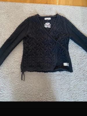 Svart omlottkofta från Odd Molly - Säljer en svart stickad omlottkofta från Odd Molly med snyggt mönster och broderad detalj på insidan. Koftan har långärmade ärmar, v-ringad hals och snörning i nederkant. Perfekt för dig som gillar unika detaljer och vill ha något extra i garderoben. Skriv om ni undrar över något❤️☺️