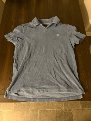 Blå kortärmad polotopp från Morris - Säljer en blå polotopp från Morris i storlek XS. Toppen har klassisk krage, korta ärmar och en liten broderad logga på bröstet. Materialet är mjukt och frottéliknande.