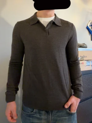 Brun polotröja i merinoull från Morris - Snygg brun polotröja från Morris i 100% merinoull. Tröjan har klassisk krage med två knappar och ribbade muddar vid ärmslut och nederkant. Perfekt för dig som gillar stilrena och bekväma plagg med lite extra kvalitet.