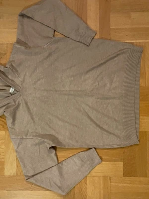 Beige hoodie från Lindex - Säljer en beige hoodie från Lindex i storlek 146/164. Tröjan har huva, ribbade muddar vid ärmslut och nederkant samt långärmad passform. Materialet är mjukt och stretchigt känns som bomull, perfekt för chill dagar. Enkel och stilren design utan mönster eller detaljer.
