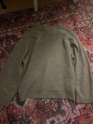 Beige stickad tröja med rund hals - Säljer en enkel och snygg beige stickad tröja med rundad hals och långa ärmar. Perfekt att slänga på sig när det är lite kyligt ute. Tröjan har en loose passform och ribbade muddar vid ärmslut och nederkant.