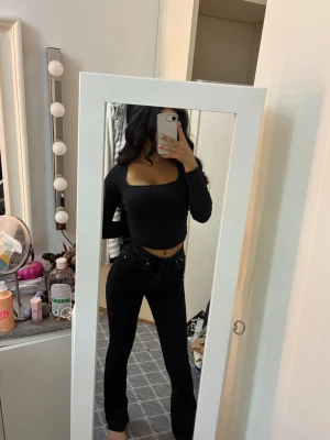 Svart ribbad croppad långärmad topp - Säljer en svart croppad topp med lång ärm och fyrkantig ringning. Toppen är ribbad och har en tight passform som framhäver figuren. Ändrat färg lite i tvätten men inget man märker. 