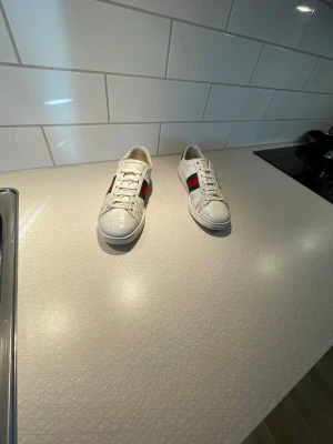 Vita guggi slides  - Ett par klina guggi slides med guggi loggan på sidan av båda skorna. Hälen där bak är detaljerad med krokodilmönster och har en fet logga under sulen på skon!