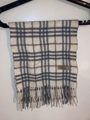 Rutig halsduk från Burberry - Snygg halsduk från Burberry i klassiskt rutigt mönster med grå och beige toner. Halsduken är tillverkad i 100% lammull och har fransar nedtill. Perfekt för detta kalla väder.