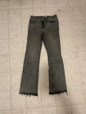 Grå bootcut jeans från Gina - Säljer ett par grå jeans från Gina Tricot i storlek 36. Modellen är bootcut. Jeansen har dragkedja och knapp framtill, och är tillverkade i jeansmaterial med en mörkgrå tvätt.