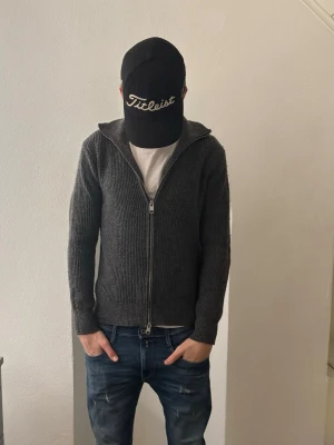 Grå stickad kofta från H&M med dragkedja - Säljer en grå stickad kofta från H&M i regular fit. Koftan har hel dragkedja framtill, ribbad struktur och långärmad design. Perfekt att slänga på sig när det är lite kyligt ute. Passar dig som gillar enkel och stilren look. Modellen är 184. 