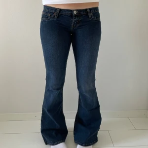 Mörkblå bootcut jeans  - Snygga mörkblå bootcut jeans med klassiska fickor och gul söm på bakfickorna. Lågmidjade och tillverkade i stretchigt denim för en bekväm passform. Perfekta för dig som gillar retrovibbar och vill ha ett par jeans med lite utsvängda ben.