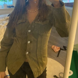 Olivgrön jeansjacka med knappar - Säljer en olivgrön jeansjacka med snygga silvriga knappar framtill och klassiska bröstfickor. Jackan har en figurnära passform och långa ärmar.