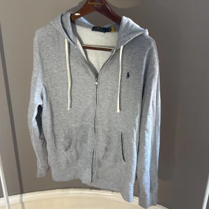 Grå zip hoodie från Ralph Lauren - Snygg grå hoodie från Polo Ralph Lauren med dragkedja och huva. Hoodien är i bra skick och perfekt nu till hösten och vintern