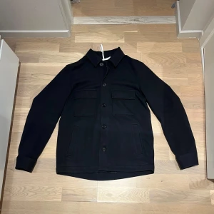 Svart overshirt med knappar Zara - . säljer en stilren svart overshirt från Zara med knappar framtill och två stora bröstfickor. Perfekt för lager-på-lager-stil och passar till många olika outfits.. Den är i väldigt bra skick 8/10 en knapp på den högra bröstfickan har gått av men borde gå att sy enkelt . Tveka inte på o fråga frågor om så behövs🤗 priset ej hugget i sten. 
