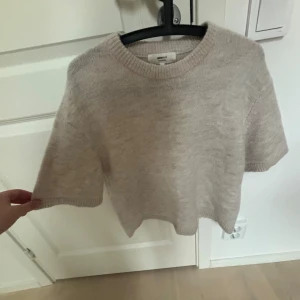 Beige stickad kortärmad tröja Ginatricot - Supermjuk beige stickad tröja från Ginatricot med korta ärmar och rund hals. Perfekt för lager-på-lager och chill vibes. Enkel och stilren design som passar till allt. Snygg ribbad kant vid hals, ärmslut och nederkant.