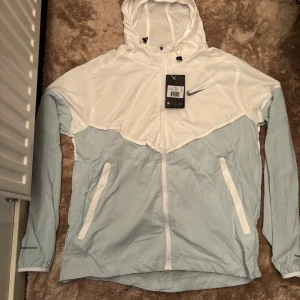 Vit o blå Nike Miller strl M - Nike vindjacka med huva i vitt och ljusblått. Jackan har hel dragkedja, två fickor framtill och justerbar huva med snörning. Swoosh-logga på bröstet och reflekterande detaljer på ärmen. Kom privat för fler bilder eller frågor aktiv varje dag‼️‼️