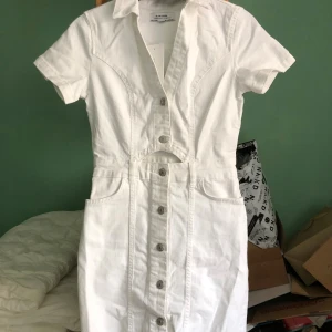 Vit jeansklänning från Chiquelle - Snygg vit jeansklänning från Chiquelle med korta ärmar, krage och knappstängning hela vägen framtill. Klänningen har cool cut-out detalj i midjan och fickor framtill. Perfekt för dig som gillar en fräsch och trendig look.