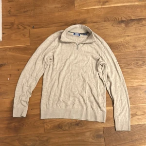 Jack & Jones halfzip - Skit snygg beige långärmad tröja från Jack & Jones med half zip-dragkedja i halsen. Tröjan är stickad och har en klassisk, enkel design med ribbade muddar och krage. Perfekt för lager-på-lager och chill stil.