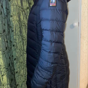 Svart dunjacka från Parajumpers M - Säljer en svart, lång och lätt dunjacka från Parajumpers med huva och dragkedja. Jackan har quiltad design, innerficka med 'security pocket' och klassisk logga på ärmen. Perfekt för kalla dagar när du vill hålla stilen.