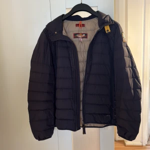 Parajumpers mörkblå lättvikts dunjacka XL - Säljer en mörkblå lättvikts dunjacka från Parajumpers i storlek XL. Jackan har quiltad design, dragkedja framtill, emblem på ärmen och snygga detaljer som gul rem vid kragen. Insidan är beige och jackan är superlätt och smidig att bära.