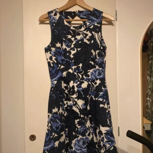 Vintage closet - Supersnygg blåvit klänning från Closet med stort blommönster, ärmlös design och markerad midja. Klänningen har en cool öppen rygg med dragkedja bak och är i ett mjukt, följsamt material. 