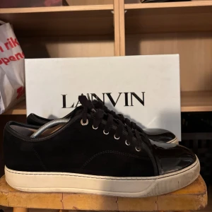 Svarta sneakers från Lanvin i mocka - Tja! Säljer ett par snygga svarta skor från Lanvin med ovandel i mocka och lackad tå. Perfekt för dig som gillar stilrena och lyxiga detaljer! De är relativt använda, absolut inte nyskick men inte heller dåligt skick. Lådan tillkommer med en dustbag. De är storlek 44 men passar bra till 45.