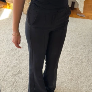 Svarta kostymbyxor med bootcut - Snygga svarta kostymbyxor med bootcut och låg midja. Byxorna har pressveck framtill, sidfickor och en bakficka. De är i ett mjukt och följsamt material som ger en clean och stilren look. Perfekta att styla med sneakers eller boots. Passar perfekt nu till hösten för en mysig men ändå snygg look. Skriv gärna!