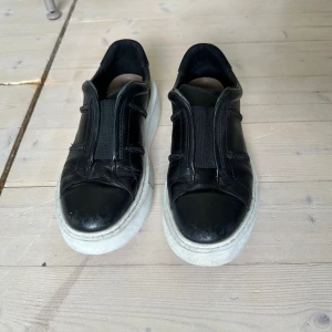 Svarta sneakers i skinn med vit sula - Svarta sneakers i skinn med vit sula och elastisk resår framtill. De är jättesköna och fotriktiga samt väldigt bra kvalitet. 