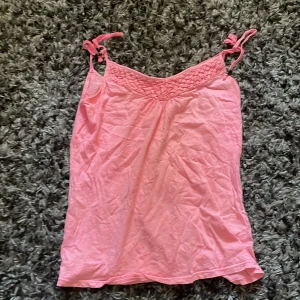 Rosa linnetopp med knytband från H&M - Säljer en söt rosa linnetopp från H&M L.O.G.G. med knytbara axelband och svarta pärldetaljer. Toppen har flätad kant upptill och är tillverkad i mjuk bomull. Perfekt för varma dagar och enkel att styla till jeans eller shorts.