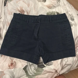 Mörkblå shorts från Zara Basic - Snygga mörkblå shorts från Zara Basic med klassisk design och raka ben. De har fickor fram och bak, hällor för bälte och stängs med dragkedja och knapp. Materialet är mjuk bomull som känns skönt mot huden. Perfekta för varma dagar och chill stil.