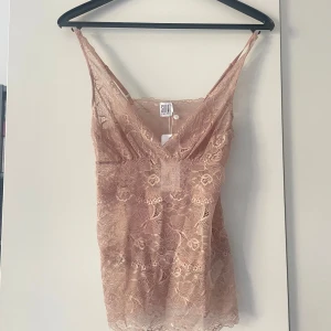 Beige rosa spetslinne från Saint Tropez - Supersnyggt beige/rosa linne från Saint Tropez i genombruten spets med v-ringning och smala axelband. Perfekt för lager på lager eller som statement-piece. Spetsen har blommigt mönster och linnet är figurnära med en feminin vibe.