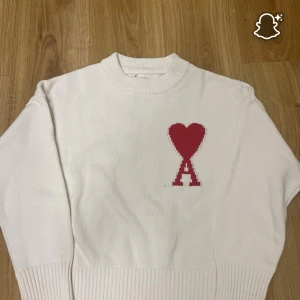 Vit stickad tröja från Ami Paris - Hej! Säljer denna tröja för att den har blivit för kort för mig är 178 men sitter bra som den ska bara att den är kortAnvänd knappt ca 4-5 gånger.Vit stickad tröja från Ami Paris med röd hjärtlogga och bokstaven A på bröstet. Tröjan har ribbade muddar och rund halsringning. Perfekt för dig som gillar stilrena plagg med en twist. Materialet är mjuk bomull. Pris kan diskuteras vid snabb och smidig affär!!