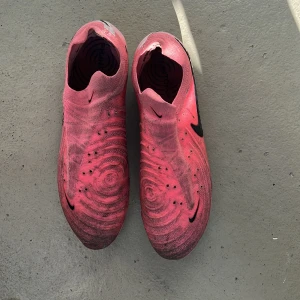 Nike Phantom GT2 rosa fotbollsskor - Säljer ett par Nike Phantom GT2 fotbollsskor i en riktigt snygg rosa färg med svarta detaljer och stora Swoosh-loggor. Skorna har en skada på den högra skon som förklarar det låga priset