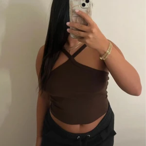 Brun croppad omlottopp - Säljer en brun croppad topp med omlottdesign och smala axelband som korsas framtill. Toppen är ärmlös och har en tight passform.