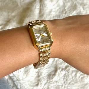 Guldig fyrkantig klocka från Ximili - Stilren klocka från Ximili med fyrkantigt ur och länkarmband i guldton. Urtavlan är silverfärgad med minimalistiska markeringar och guldiga visare. Klockan har en klassisk och elegant design som sticker ut på handleden.