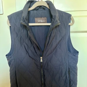 Mörkblå dunväst Oscar Jacobson - Mörkblå dunväst från Oscar Jacobson. Västen har ett stilrent rutmönster och är perfekt att slänga över en hoodie eller t-shirt. Snygg och enkel design som funkar till många outfits, perfekt nu inför hösten. Killen på bilden är 178.