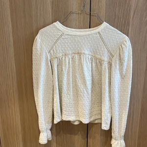 Vit blus med spetsdetaljer från Zara - Supersöt vit blus från Zara med långärmad design och fina spetsdetaljer längs axlar och bröst. Blusen har lätt struktur i tyget och volang vid ärmslut. Perfekt för dig som gillar romantisk och stilren look.