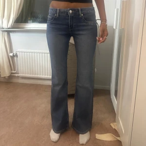 Blå bootcut jeans med låg midja - Snygga blå jeans med bootcut-modell och låg midja. Jeansen har klassisk femficksdesign, dragkedja och knapp framtill. Materialet är mjukt denim som sitter skönt och ger en clean look. Perfekta för dig som gillar en tidlös och trendig stil.