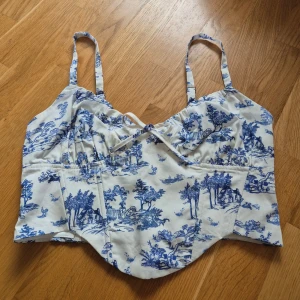 Vit och blå korsettopp från Bershka - Superfin korsettopp från Bershka. HELT NY MED LAPPAR KVAR‼️ Den har söt knytdetalj framtill och smockad rygg med dragkedja. Gjord i en linnemix som känns sval och fräsch.