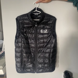Svart dunväst från EA7 - -Svart dunväst från EA7 Emporio Armani.                          -Nyskick, köptes för ett tag sen men knappt används -Köptes på Zalando eller Boozt så helt äkta.                                         -Ställ gärna frågor och fler bilder kan skickas😊
