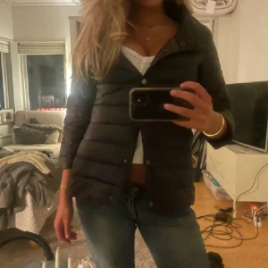 Henri liknade jacka - Svart, lätt quiltad dunjacka från Amisu med raka, trekvartsärmar och rundad krage. Jackan har knäppning med silvriga knappar framtill. Perfekt för lager-på-lager och enkel att styla till olika outfits.