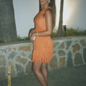 Orange kortklänning med fransar - Säljer en superfin orange kortklänning med ärmlös design och fransar på kjolen. Klänningen har en tight passform upptill och är perfekt för dig som vill sticka ut med färg och coola detaljer. Perfekt för sommarkvällar eller när du vill ha något extra.