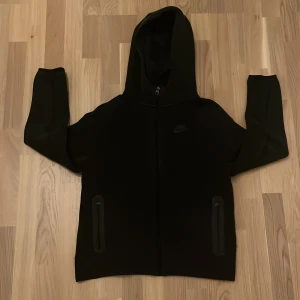 Svart Nike hoodie med dragkedja junior xl - Svart hoodie från Nike i storlek XL med hel dragkedja framtill och två fickor med dragkedja. Klassisk Nike-logga på bröstet och huva. Perfekt för chill eller träning, riktigt clean och enkel stil.