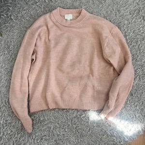 Ljusrosa stickad tröja H&M - Supermysig ljusrosa stickad tröja från H&M med rund halsringning och ribbade muddar. Tröjan har en relaxed passform och är perfekt att slänga på sig när det är kyligt ute. Enkel och stilren design som funkar till allt.