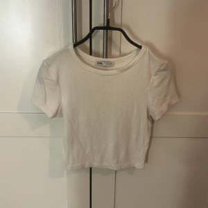 Vit croppad t-shirt från Zara - En basic vit croppad t-shirt från Zara med rund halsringning och korta ärmar. Enkel och stilren modell i mjuk bomull, perfekt att matcha med jeans eller kjol för en clean look.