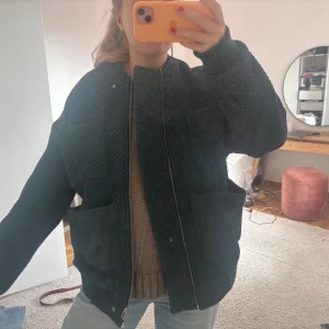 Mörkgrön quiltad bomberjacka - Säljer en mörkgrön quiltad bomberjacka med oversized passform. Jackan har stora fickor framtill, dragkedja och ribbade muddar vid ärmslut och hals. Perfekt för dig som gillar en chill och trendig look.