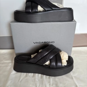 Svarta platåsandaler från Vagabond - Helt oanvända nya snygga svarta sandaler från Vagabond med breda, korslagda remmar i skinn och chunky platåsula. Perfekta för dig som gillar en modern och edgy look. Stilren design med rund tå och plattformsula som ger extra höjd utan att tumma på komforten. Nypris 1000:-  !!Finns på fler sidor!!