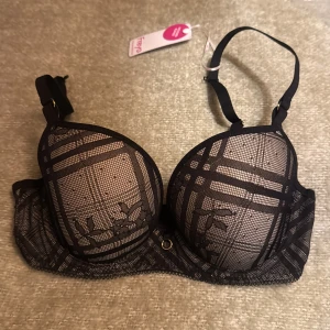 Svart Bh  Freya 60F - Säljer en bh  från Freya med coolt rutigt spetsmönster och blommiga detaljer. Justerbara axelband och guldfärgade ringar framtill. Materialet är en mix av spets och syntet, vilket ger en lyxig känsla och snygg passform.