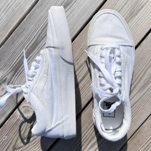 Vita Vans Old Skool - Klassiska Vans Old Skool sneakers i helvitt med lågt skaft, rund tå och platt sula. Skorna har snörning och är tillverkade i canvas och syntet med den ikoniska sidoremsan. Perfekta för en clean och stilren look. Använda 3 gånger. Önskar du veta exakta mått? Tveka inte att höra av dig!