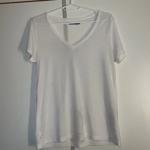 Vit v-ringad t-shirt från Vero Moda - Enkel och stilren vit t-shirt från Vero Moda med v-ringning och korta ärmar. Tillverkad i en mjuk blandning av polyester och viskos som ger en skön känsla. Perfekt basplagg med normal passform och klassisk look.
