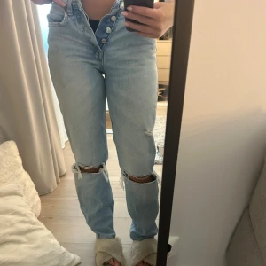Ljusblå jeans från Zara - Säljer ett par ljusblå jeans från Zara med raka ben och slitna detaljer vid knäna. Byxorna har medelhög midja, knäppning med fyra silverfärgade knappar och klassisk femficksdesign. Så så fina men tyvärr för små för mig!🩷