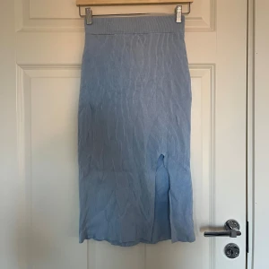 Ljusblå ribbad långkjol från H&M - Säljer en ljusblå, ribbad långkjol från H&M i storlek XS. Kjolen har en hög midja, stretchigt stickat material och en slits framtill som ger en snygg detalj. Perfekt för dig som gillar enkel men stilren design.